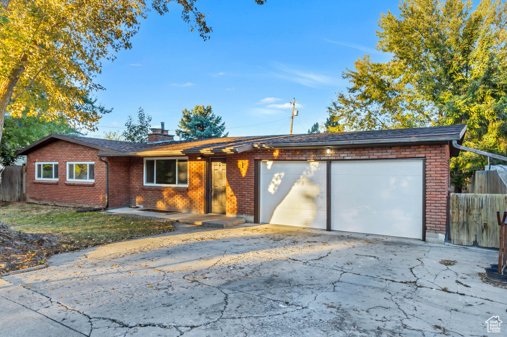 Single story home featuring an attached garage, fence, driveway, brick siding, and a chimney