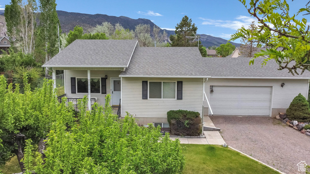 View of front of property featuring a garage, gravel driveway, roof with shingles, and a mountain view