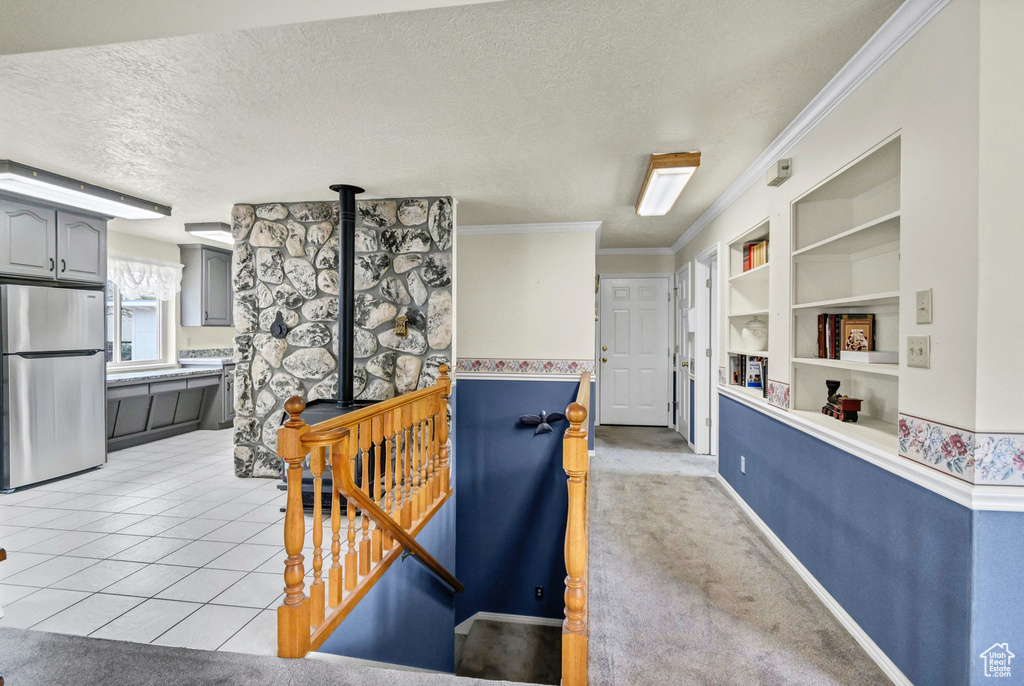 Hallway featuring a textured ceiling, built in shelves, ornamental molding, and light tile patterned floors