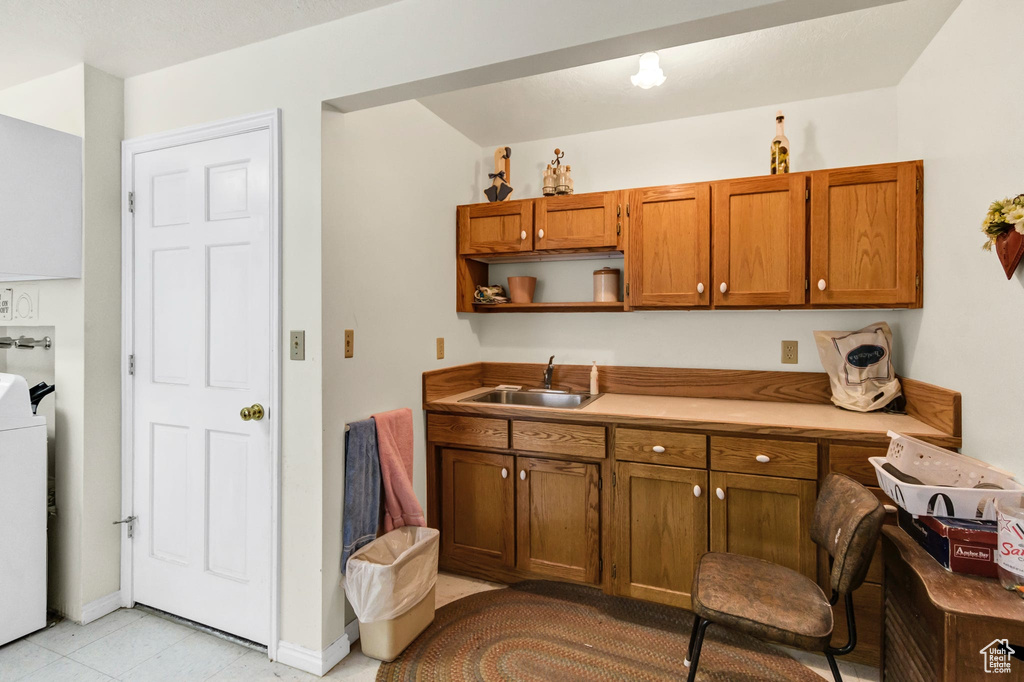 Kitchen featuring a sink, brown cabinetry, open shelves, washer / dryer, and light countertops
