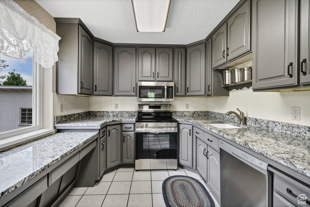 Kitchen featuring stainless steel appliances, a sink, light stone counters, and light tile patterned floors