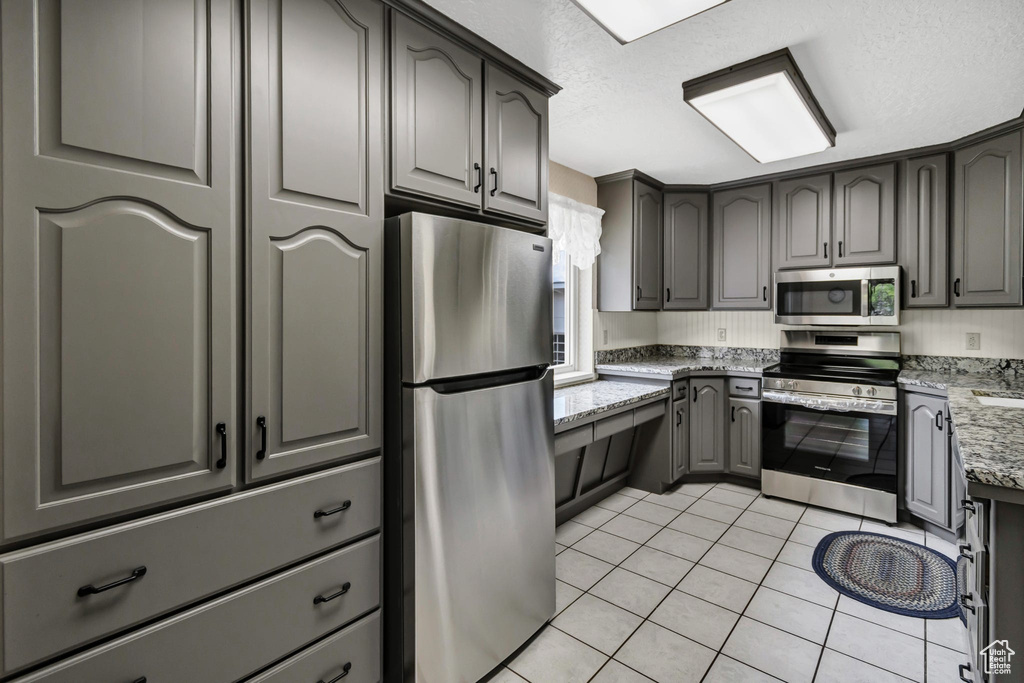 Kitchen with appliances with stainless steel finishes, light tile patterned floors, light stone counters, gray cabinetry, and a textured ceiling