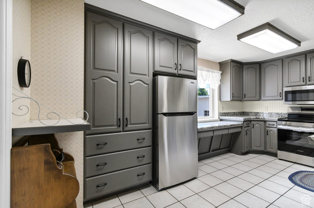 Kitchen featuring stainless steel appliances, gray cabinets, light stone countertops, light tile patterned floors, and a textured ceiling