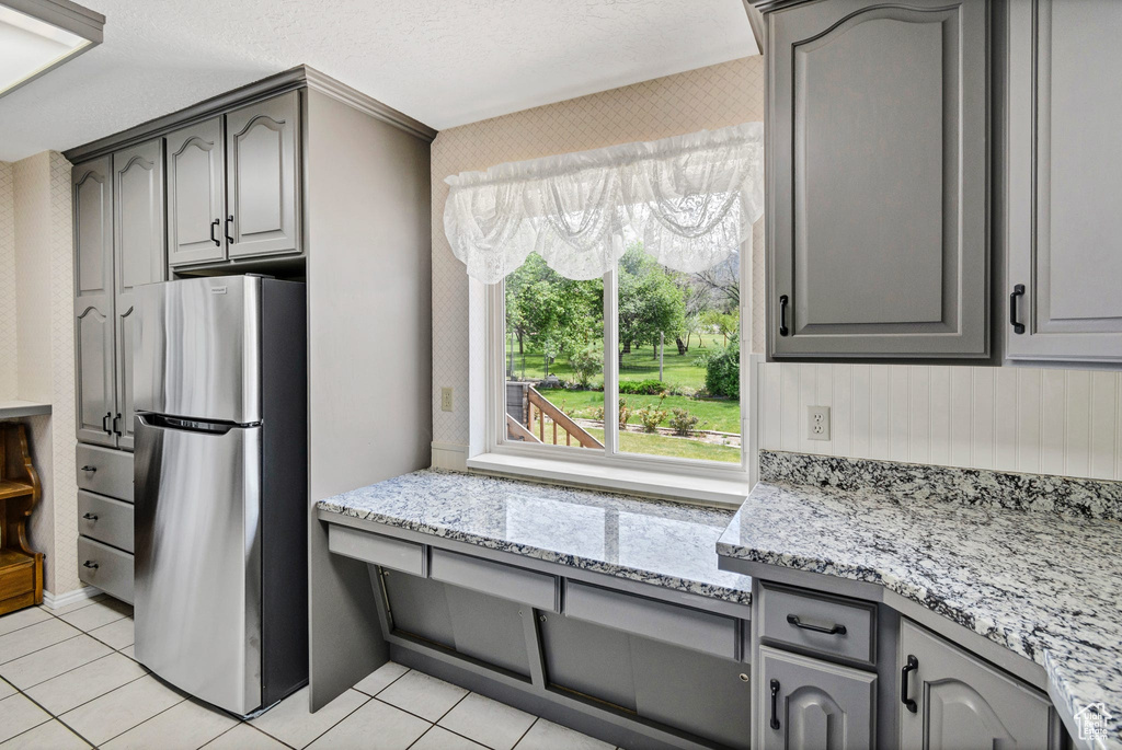 Kitchen featuring freestanding refrigerator, gray cabinetry, and light tile patterned flooring