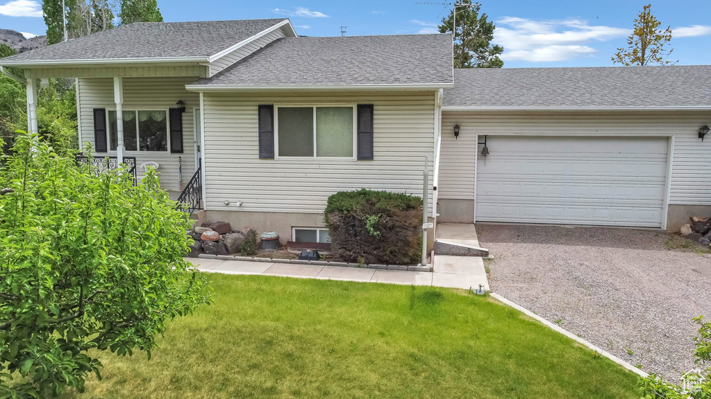 View of front of home featuring gravel driveway, a front lawn, a garage, and roof with shingles
