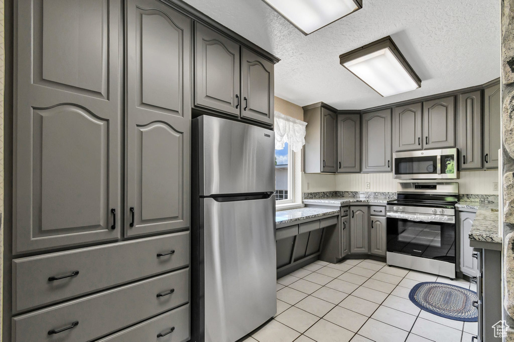 Kitchen featuring appliances with stainless steel finishes, gray cabinets, light tile patterned flooring, a textured ceiling, and light stone countertops
