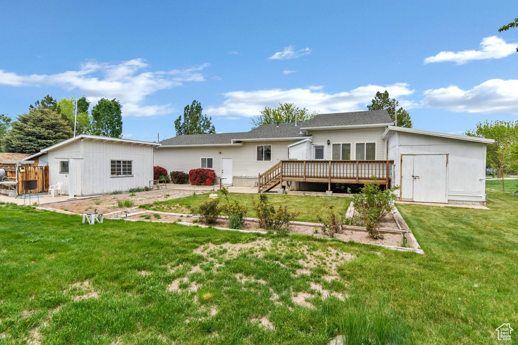Back of property with a deck, an outdoor structure, a storage unit, a yard, and a vegetable garden
