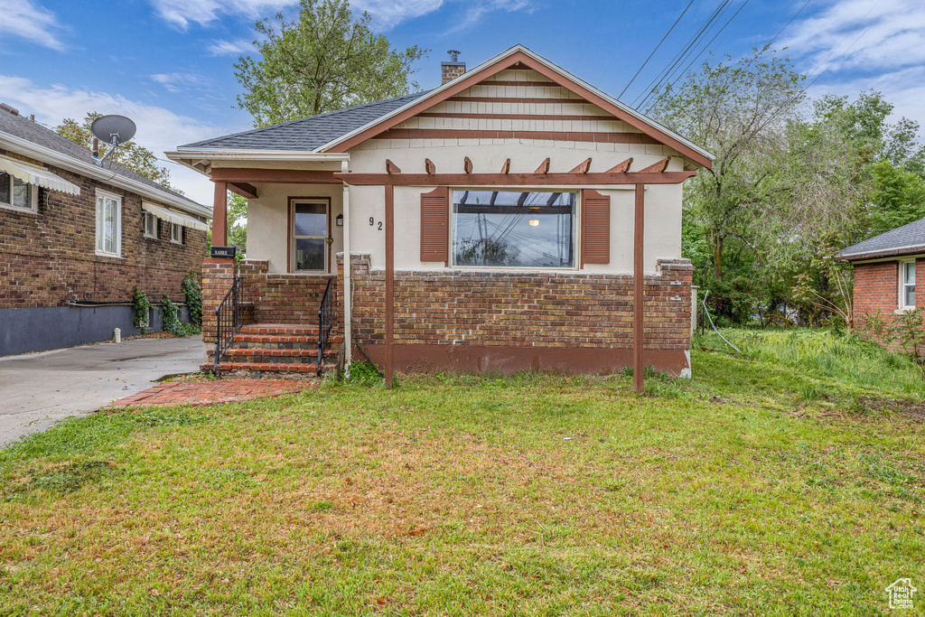 Bungalow-style house with stucco siding, a front yard, covered porch, and a chimney