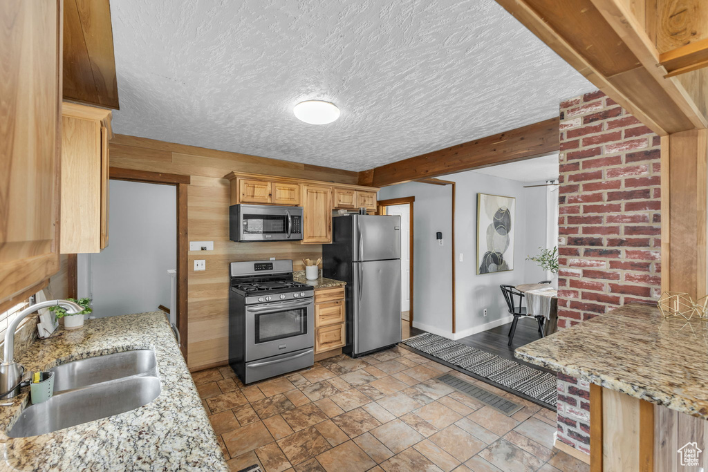 Kitchen with stainless steel appliances, a sink, baseboards, light brown cabinets, and stone finish flooring