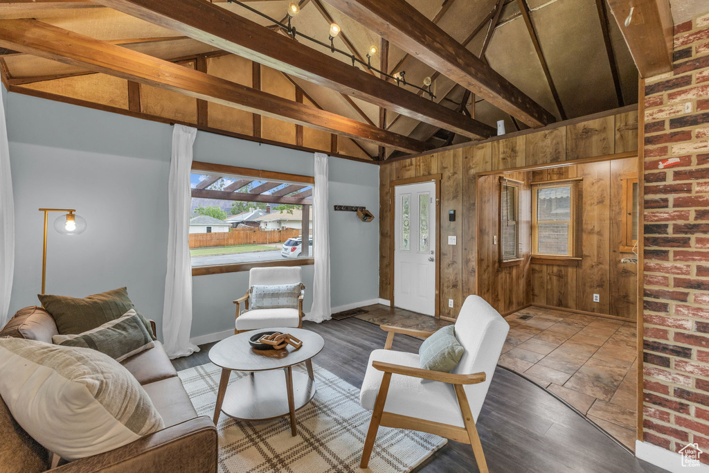 Living area with beamed ceiling, wood walls, wood finished floors, baseboards, and high vaulted ceiling