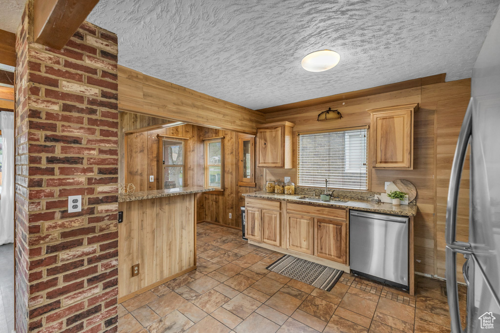Kitchen with stainless steel appliances, a sink, wood walls, a textured ceiling, and light stone countertops