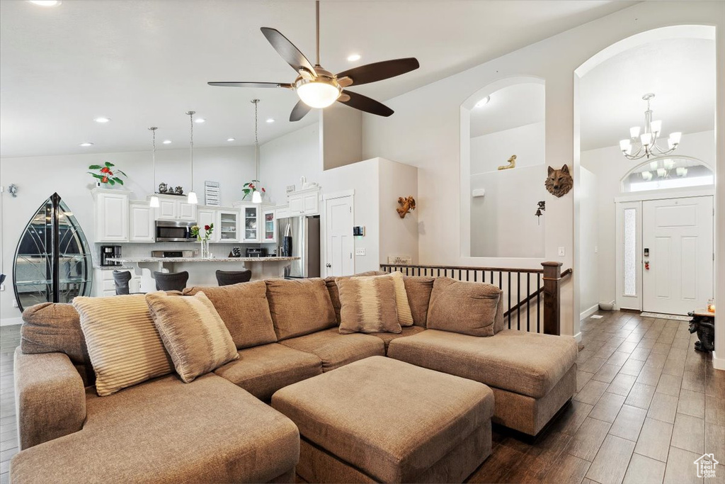 Living room with high vaulted ceiling, a ceiling fan, a chandelier, arched walkways, and baseboards