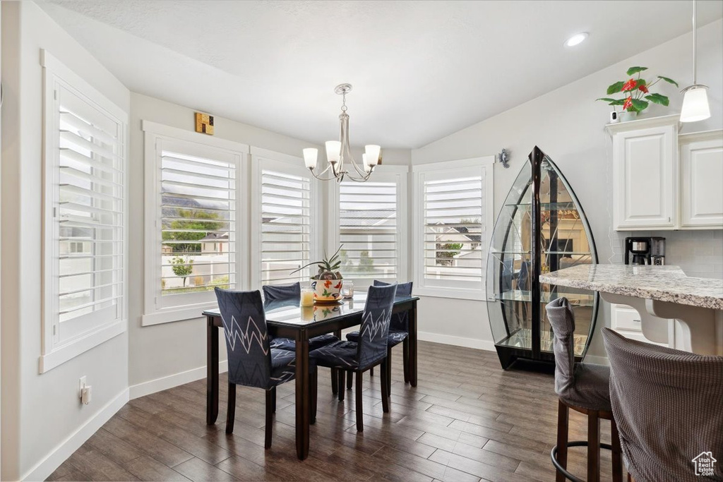 Dining area featuring a chandelier, healthy amount of natural light, dark wood-style floors, baseboards, and vaulted ceiling