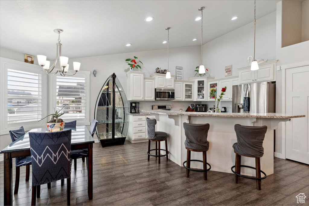 Kitchen featuring stainless steel appliances, a chandelier, a kitchen breakfast bar, dark wood-style floors, and glass insert cabinets