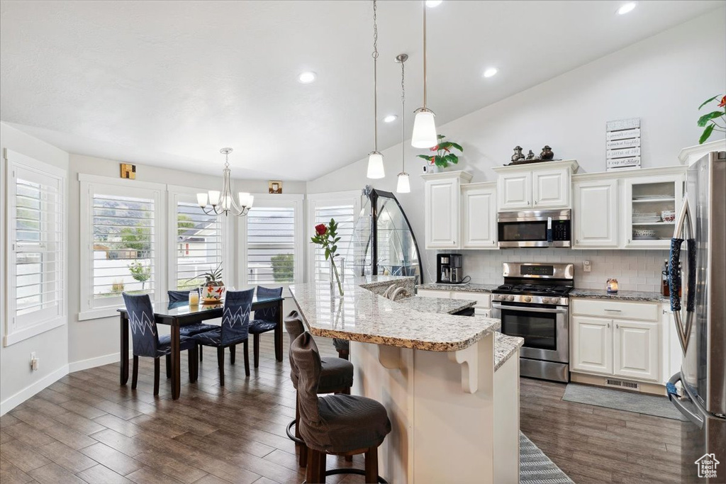 Kitchen with appliances with stainless steel finishes, a chandelier, vaulted ceiling, backsplash, and a kitchen breakfast bar