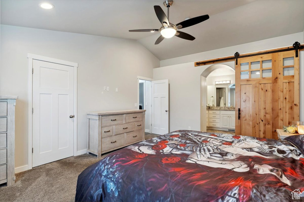 Carpeted bedroom with vaulted ceiling, a barn door, ensuite bath, baseboards, and ceiling fan