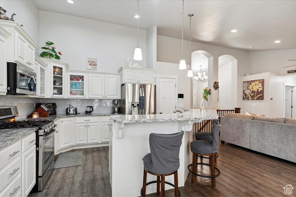 Kitchen featuring stainless steel appliances, a kitchen breakfast bar, dark wood-style flooring, open floor plan, and a towering ceiling