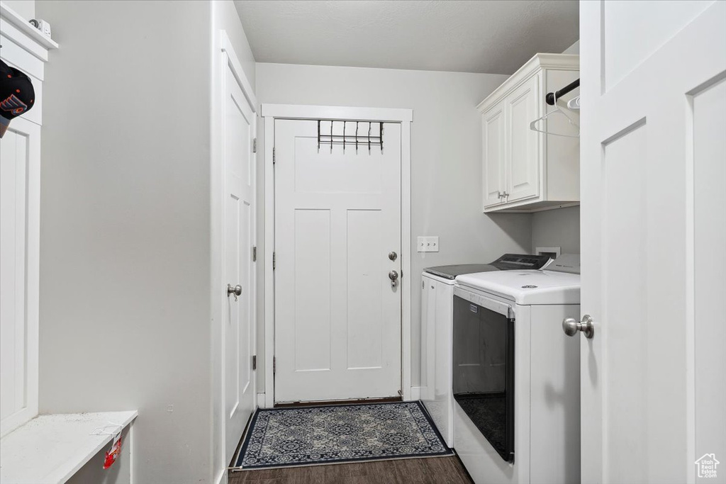 Clothes washing area featuring washing machine and dryer, cabinet space, wood finished floors, and baseboards