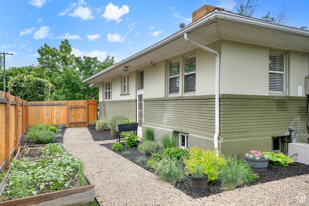View of property exterior with a gate, a fenced backyard, a garden, and stucco siding