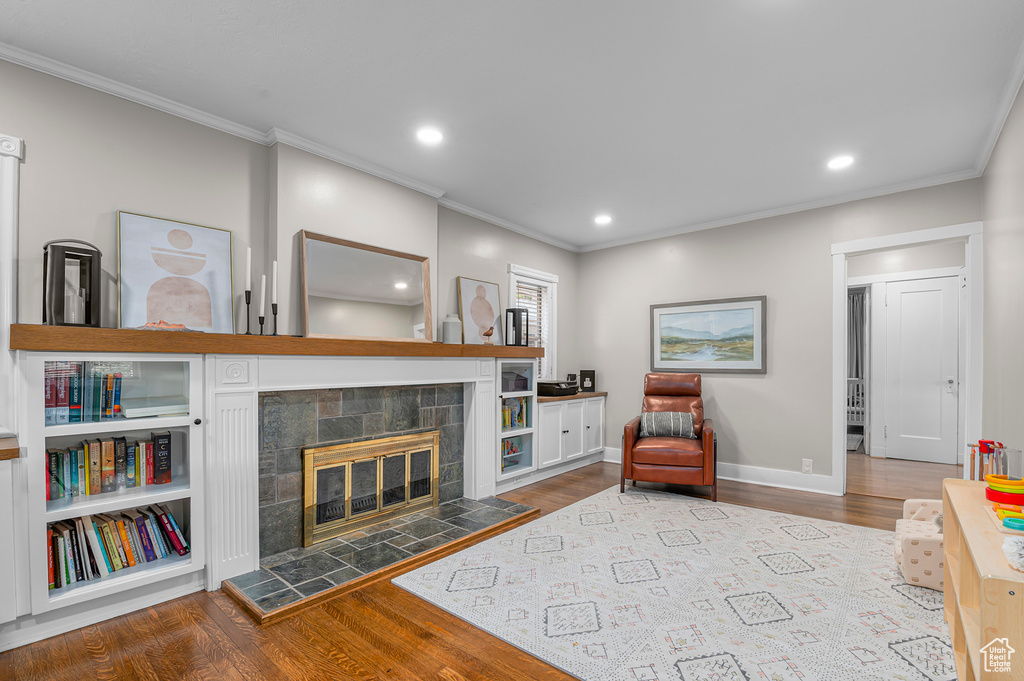 Living room with crown molding, wood finished floors, a tiled fireplace, baseboards, and recessed lighting