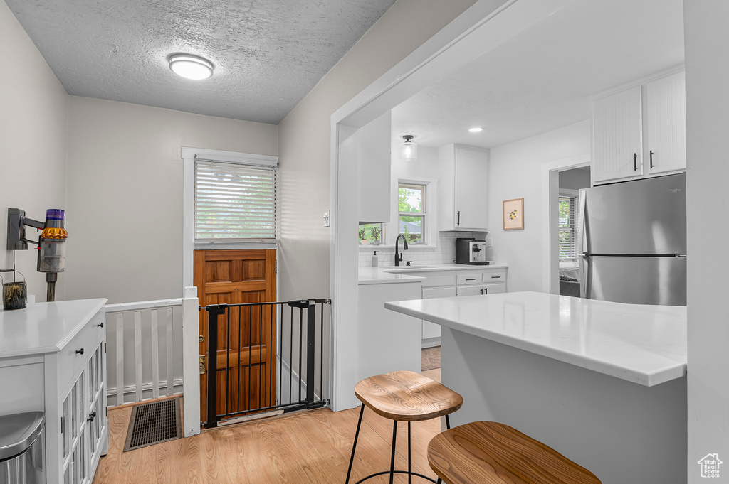 Kitchen featuring freestanding refrigerator, light wood-type flooring, a sink, white cabinets, and a kitchen breakfast bar