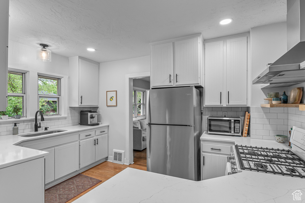 Kitchen with stainless steel appliances, a sink, wall chimney exhaust hood, plenty of natural light, and recessed lighting