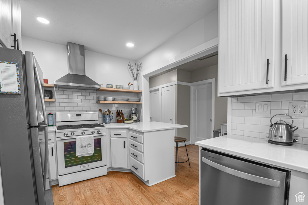 Kitchen with appliances with stainless steel finishes, wall chimney range hood, open shelves, a peninsula, and tasteful backsplash