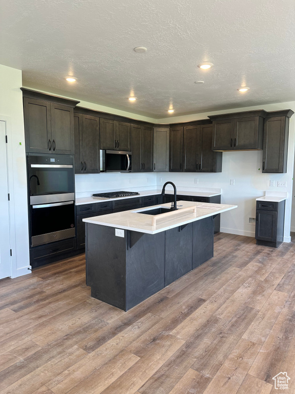 Kitchen featuring a sink, appliances with stainless steel finishes, wood finished floors, baseboards, and light countertops