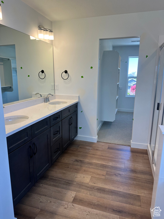 Bathroom featuring wood finished floors, baseboards, double vanity, and a shower stall