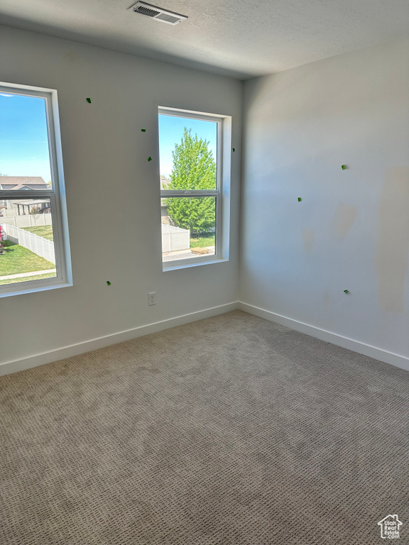 Empty room with carpet, baseboards, and a textured ceiling
