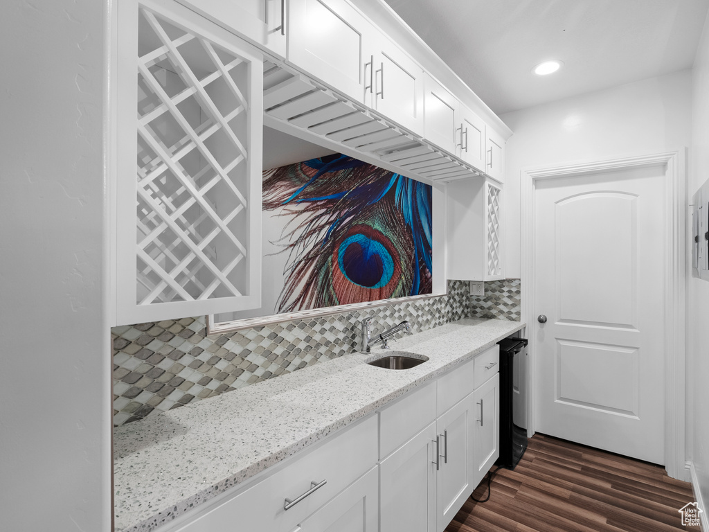 Kitchen featuring a sink, white cabinetry, tasteful backsplash, light stone countertops, and dark wood-type flooring