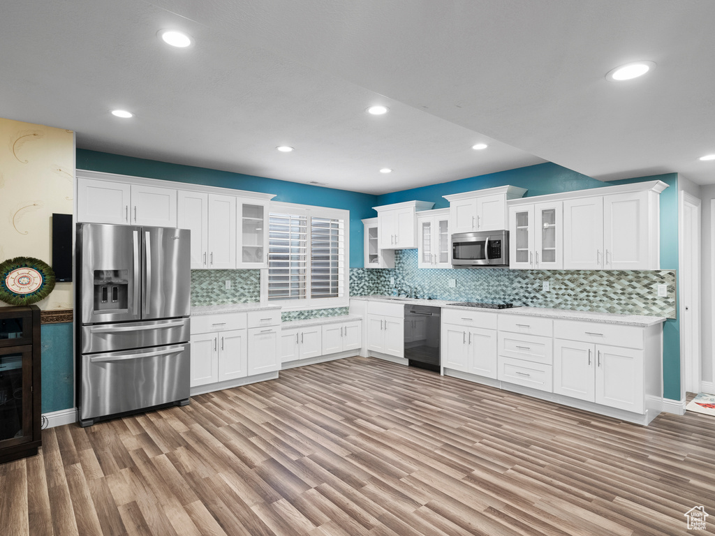 Kitchen with black appliances, light countertops, light wood-style floors, white cabinets, and tasteful backsplash