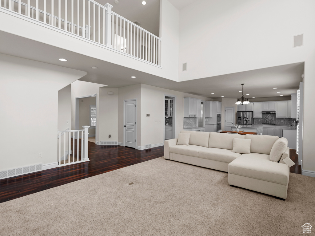 Living area with dark colored carpet, a chandelier, a high ceiling, recessed lighting, and dark wood finished floors