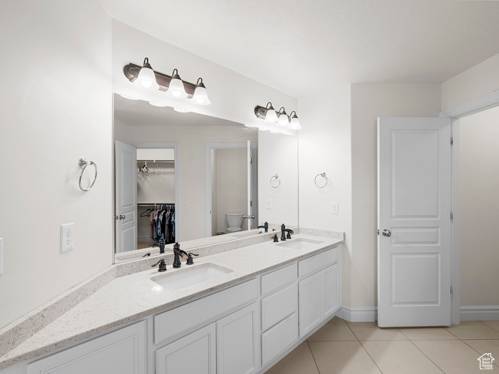 Full bath featuring tile patterned floors, toilet, double vanity, a walk in closet, and baseboards