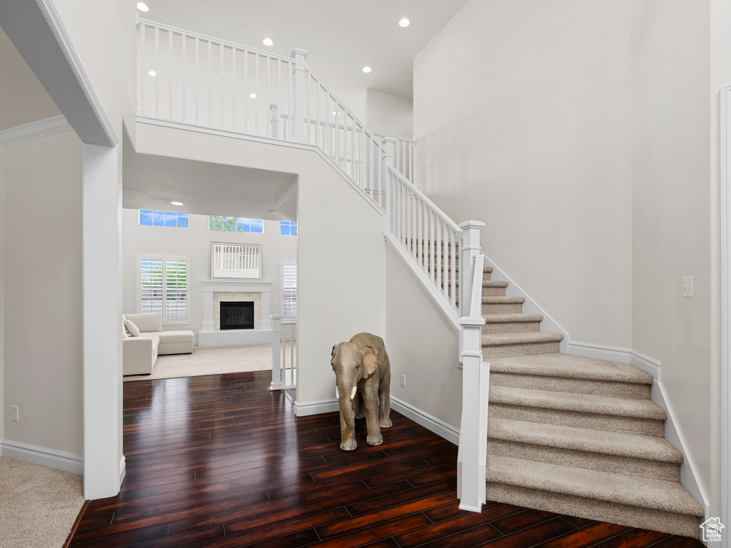 Staircase with wood finished floors, a towering ceiling, baseboards, recessed lighting, and a premium fireplace