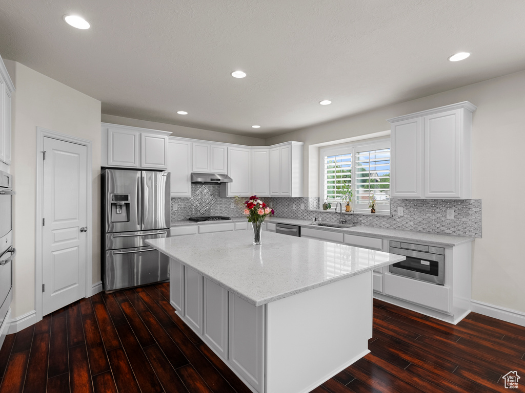 Kitchen featuring appliances with stainless steel finishes, under cabinet range hood, a sink, a kitchen island, and dark wood-style flooring
