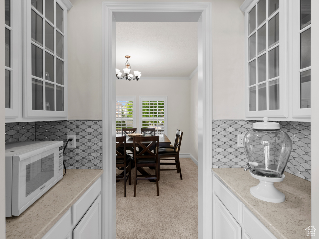 Kitchen featuring white microwave, tasteful backsplash, white cabinetry, ornamental molding, and glass insert cabinets
