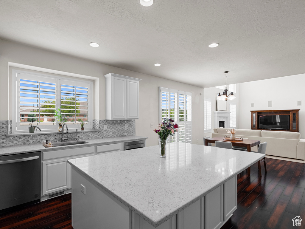 Kitchen featuring dishwasher, a sink, dark wood-style floors, decorative backsplash, and a center island