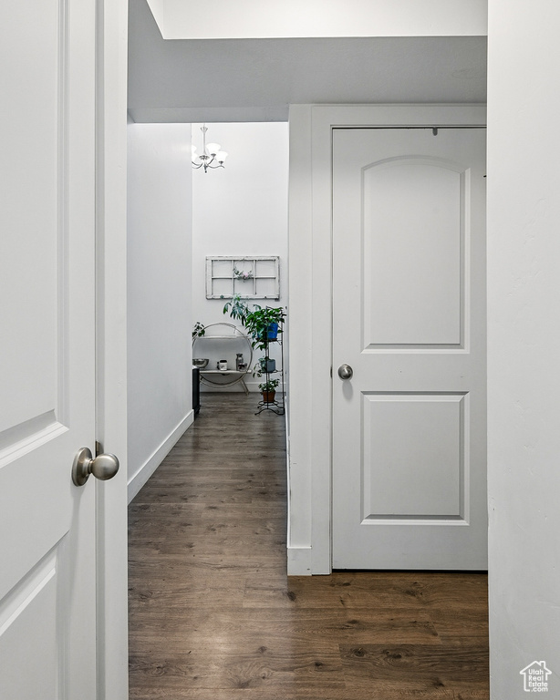 Hallway with dark wood-type flooring, a chandelier, and baseboards