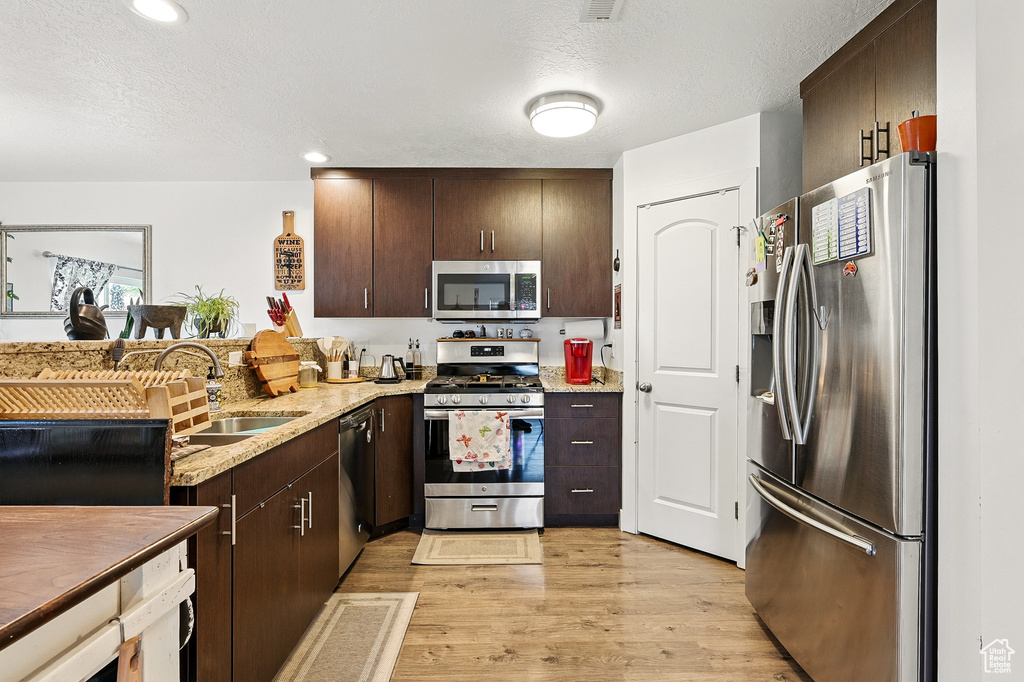 Kitchen with stainless steel appliances, a sink, dark brown cabinets, light wood finished floors, and a textured ceiling