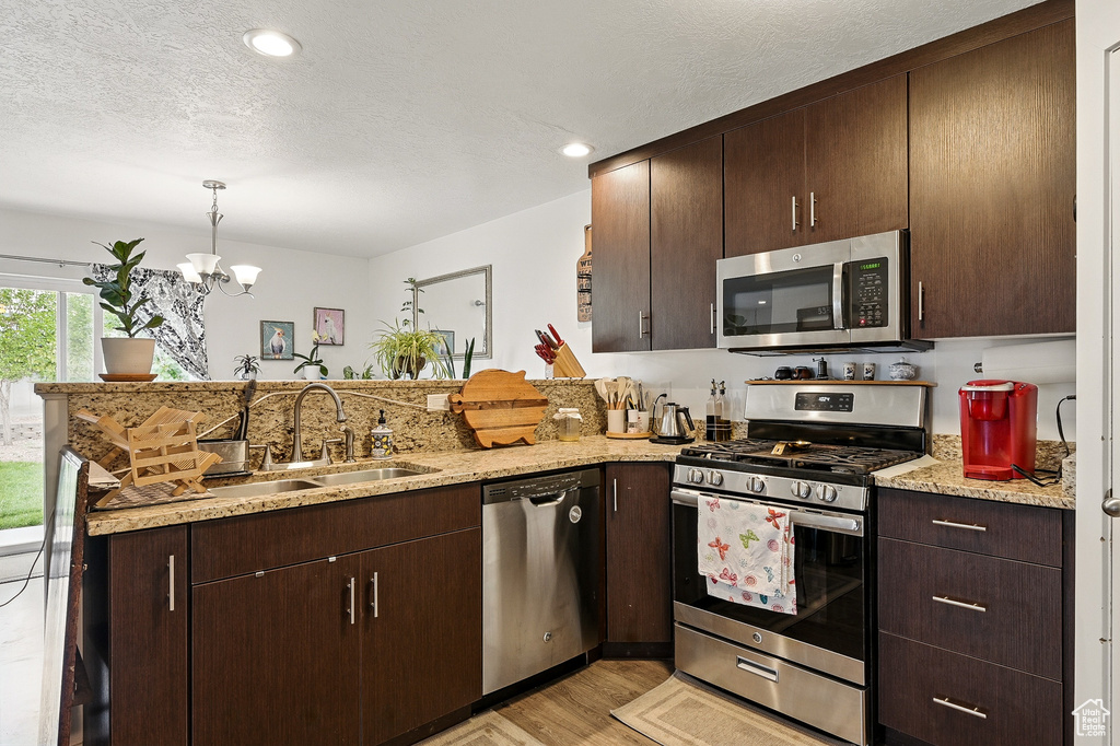Kitchen featuring appliances with stainless steel finishes, a sink, a peninsula, a chandelier, and light wood-style floors