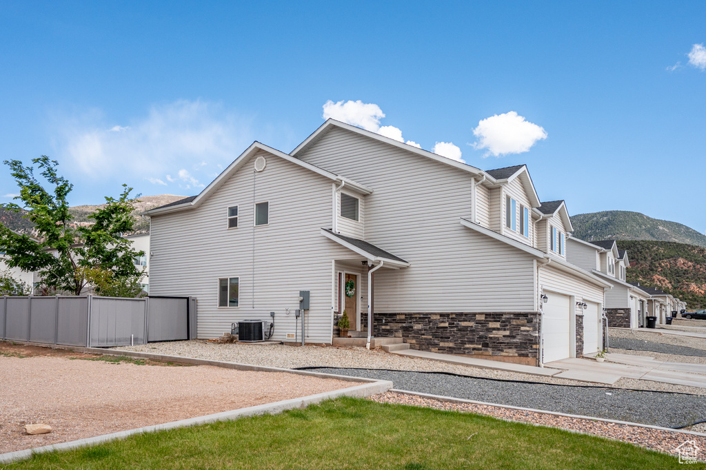 View of side of home featuring central air condition unit, driveway, a garage, fence, and a mountain view