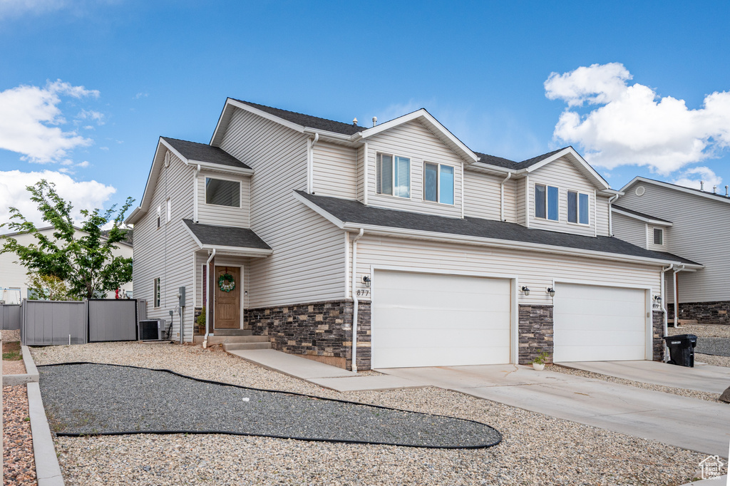 View of front facade featuring a garage, concrete driveway, fence, stone siding, and cooling unit