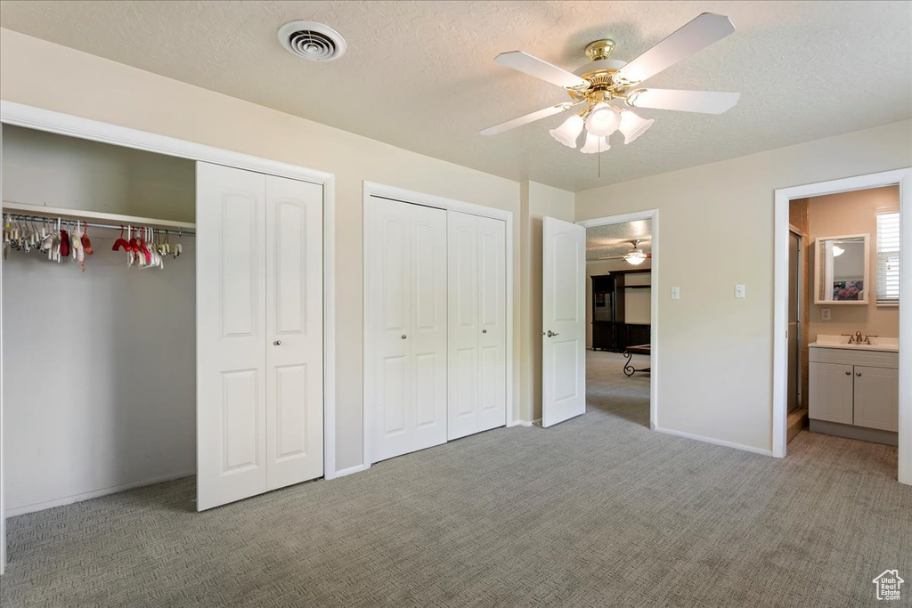Unfurnished bedroom featuring light colored carpet, multiple closets, a textured ceiling, baseboards, and a sink