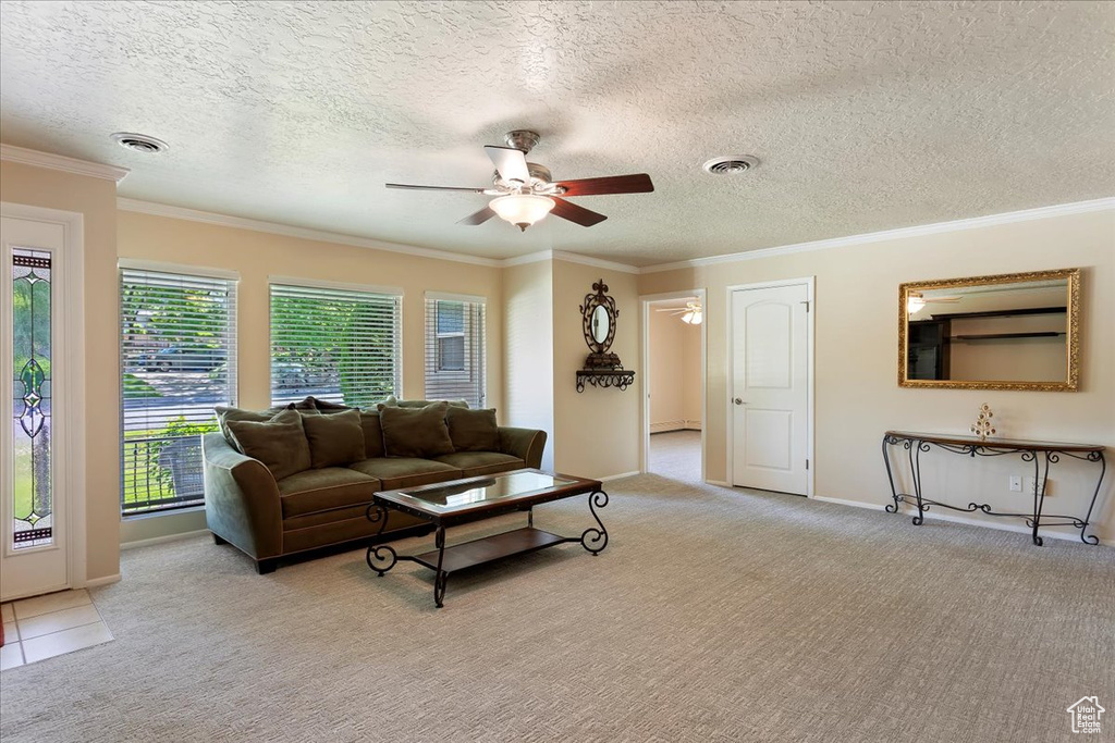 Living room featuring light carpet, a ceiling fan, ornamental molding, a textured ceiling, and baseboards