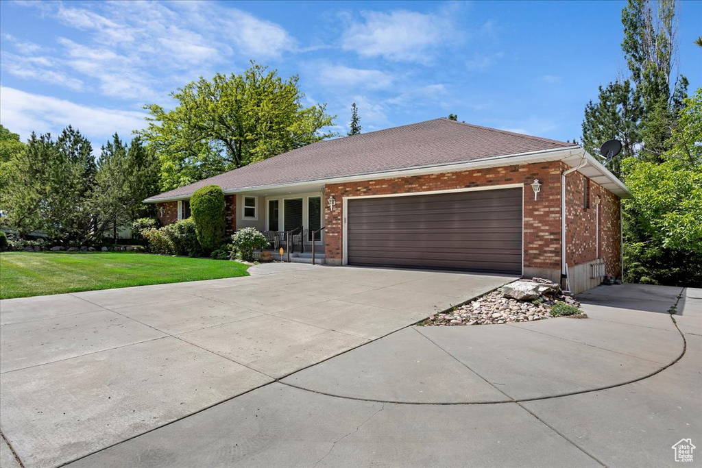 Ranch-style home featuring concrete driveway, brick siding, a front lawn, and an attached garage
