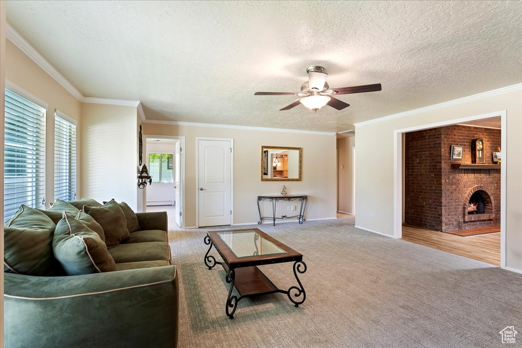 Carpeted living area with a ceiling fan, a fireplace, a textured ceiling, ornamental molding, and baseboards