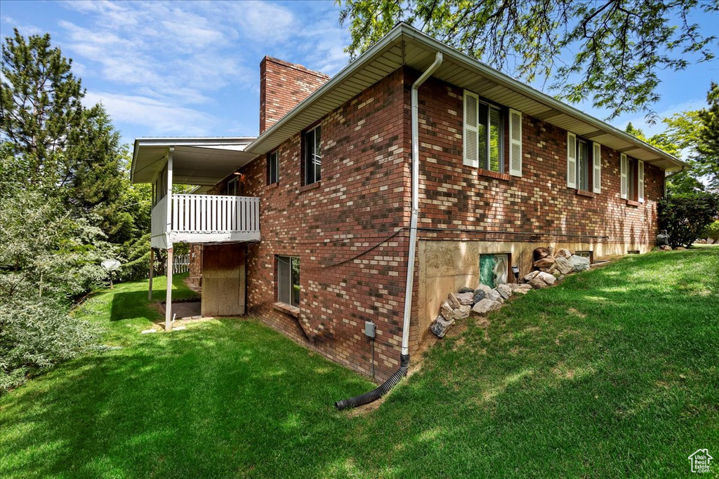 View of property exterior with a chimney, a lawn, and brick siding