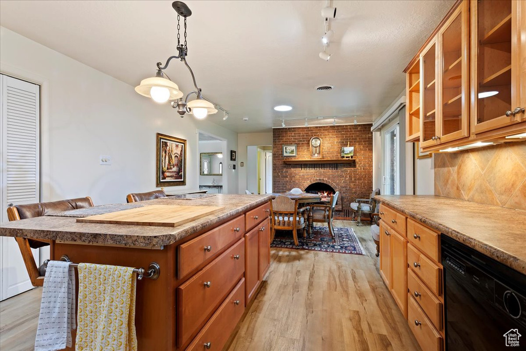 Kitchen with track lighting, dishwasher, light wood finished floors, a center island, and a fireplace