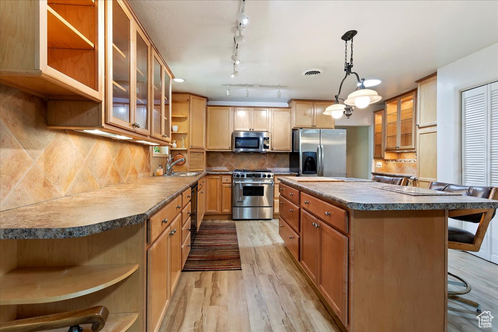 Kitchen with open shelves, appliances with stainless steel finishes, light wood finished floors, a center island, and a sink